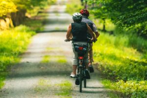 Rückansicht von zwei Radfahrern mit Helmen, die auf einem schattigen Waldweg fahren.